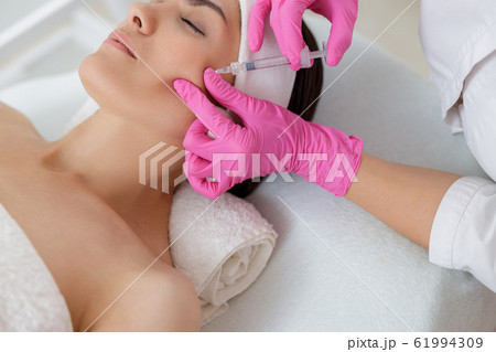 Beautician making injection in lady cheek at spa salon 61994309