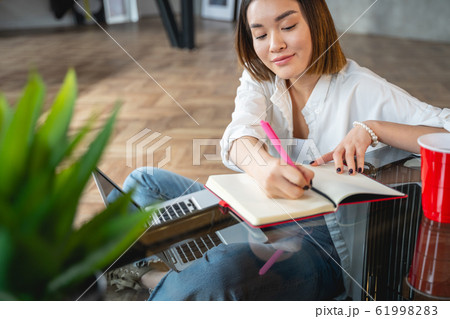 Busy attractive Asian woman making notes indoors Busy attractive Asian woman making notes indoors 61998283