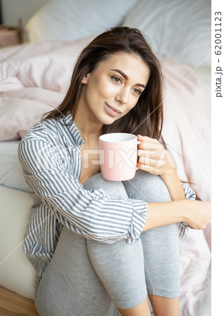 Dreamy young woman sitting by the bed Dreamy young woman sitting by the bed 62001123