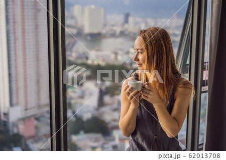 Young woman is drinking coffee in the morning on the background of a window with a sea view 62013708