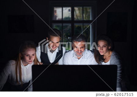 Group of businesspeople with computer indoors in office, working late. Group of businesspeople with computer indoors in office, working late. 62017515