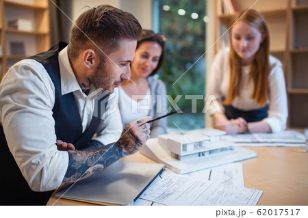 Group of architects with model of house sitting indoors in office, working. Group of architects with model of house sitting indoors in office, working. 62017517