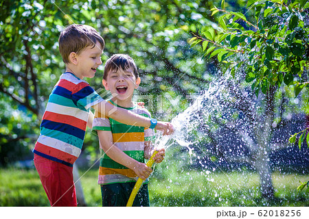 Cute little boy watering plants with watering hose 62018256