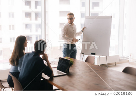 Young confident businessman presenting new project to partners on whiteboard 62019130
