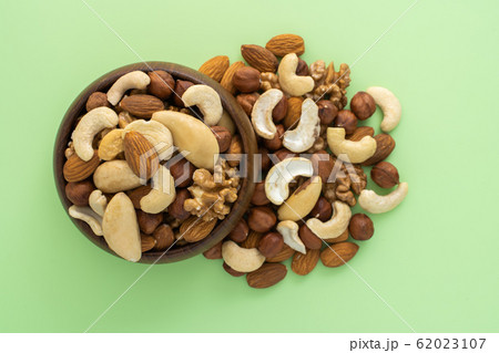 Different nuts in wooden bowl on green background Different nuts in wooden bowl on green background 62023107