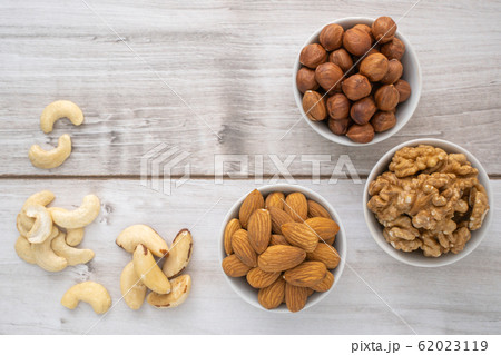 Different nuts in white bowls on wood table 62023119
