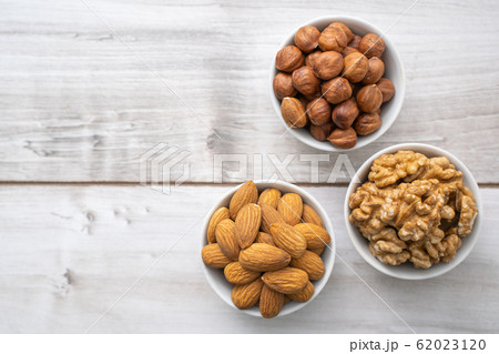 Different nuts in white bowls on wood table 62023120