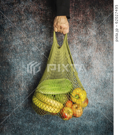 A man's hand holds a green string bag with fresh 62027495