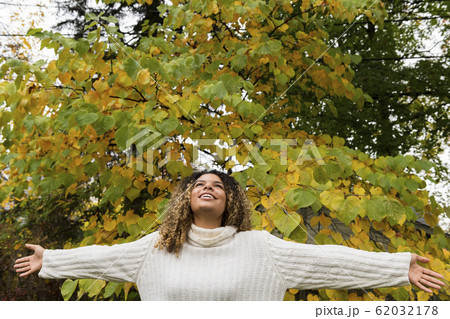 Smiling woman with her arms outstretched by tree 62032178