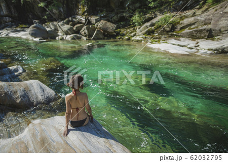 Woman wearing bikini sitting on rock by river Woman wearing bikini sitting on rock by river 62032795