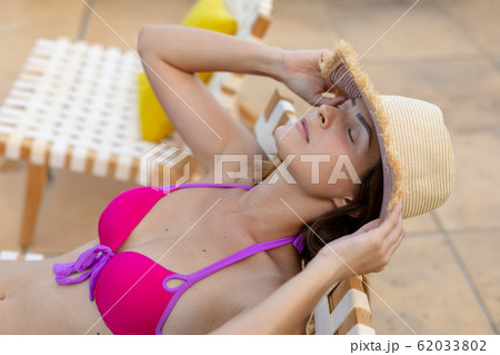 Young woman relaxing near swimming pool on a sunny day Young woman relaxing near swimming pool on a sunny day 62033802