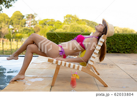 Young woman relaxing near swimming pool on a sunny day Young woman relaxing near swimming pool on a sunny day 62033804