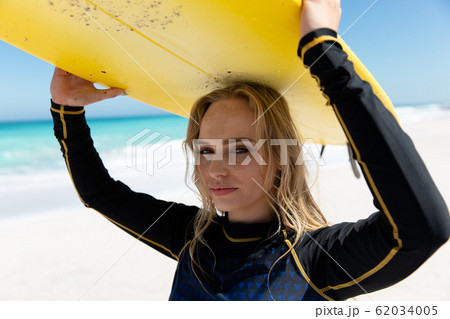 Young woman carrying a surfboard at the beach 62034005