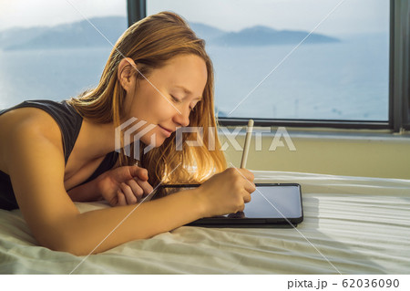 Young woman draws on a tablet against the background of a window with a sea view. Designer Young woman draws on a tablet against the background of a window with a sea view. Designer 62036090