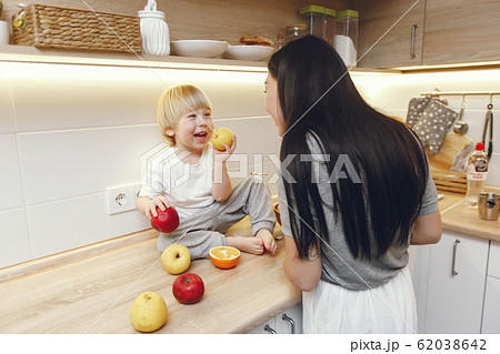 Mother with little son eating fruits in a kitchen Mother with little son eating fruits in a kitchen 62038642