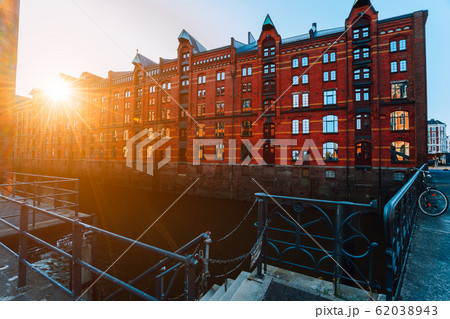 A red brick multi-storey houses of Speicherstadt Hamburg. Famous landmark of old red brick buildings in golden sunset light. Scenic evening view with canal handrail in foreground 62038943