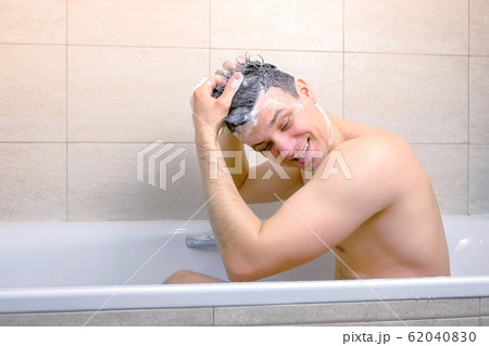 Man is washing his head with shampoo and making a Mohawk from hairs sitting in bathtub. Man is washing his head with shampoo and making a Mohawk from hairs sitting in bathtub. 62040830