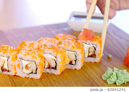 Man is eating rolls with wood sticks, wasabi, ginger and soy sauce. Hand close-up. Man is eating rolls with wood sticks, wasabi, ginger and soy sauce. Hand close-up. 62041241