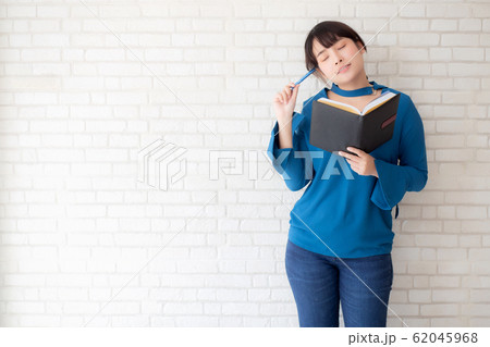 Beautiful asian woman smiling standing thinking and writing notebook on concrete cement 62045968