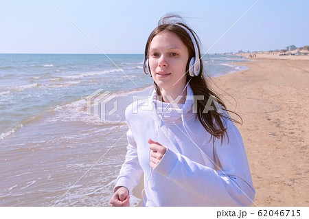 Woman in headphones music jogging at sea sand beach sport run outdoor training. 62046715