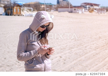 Young woman is typing on phone on the beach by sea. 62047304