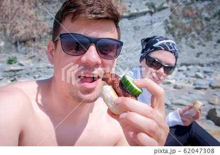 Man blogger is eating shashlik with bread and cucumber on camera with his wife and talking about it his subscribers. 62047308