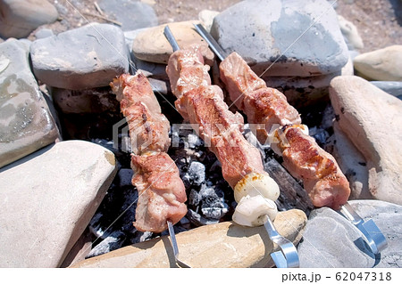 Shashlik cooking on skewers on stone handmade campfire with hot charcoals. Shashlik cooking on skewers on stone handmade campfire with hot charcoals. 62047318