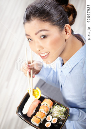 Beautiful young woman eating sushi. Shallow depth 62047983