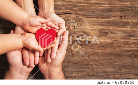 family hands holding red heart on wooden background. Donation, charity, health concept. family hands holding red heart on wooden background. Donation, charity, health concept. 62050859
