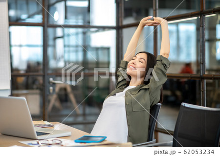 Long-haired brunette asian girl sitting at the table and stretching Long-haired brunette asian girl sitting at the table and stretching 62053234