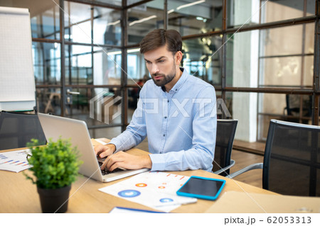 Bearded man in a blue shirt sitting in the office and working on laptop 62053313