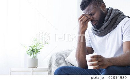 Black man with flu warming with cup with hot tea at home Black man with flu warming with cup with hot tea at home 62054980