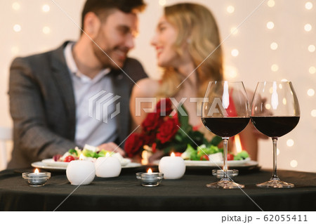 Affectionate couple dating in restaurant, glasses with red wine in foreground 62055411