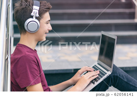 Smiling teenage boy with a laptop on the street. 62056141