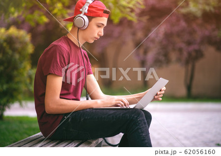 Teenage boy with a laptop in the park. Handsome Teenage boy with a laptop in the park. Handsome 62056160