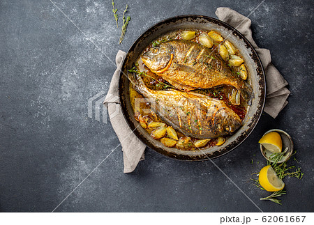 Baked sea bream or dorada with onion and herbs in pan on dark background 62061667