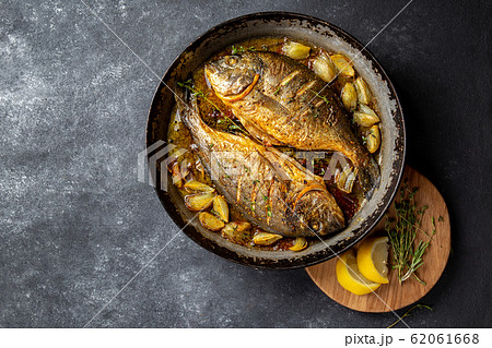 Baked sea bream or dorada with onion and herbs in pan on dark background Baked sea bream or dorada with onion and herbs in pan on dark background 62061668