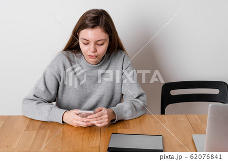 A teenage girl sits at the wooden table and procrastinating in social media. Addiction problem 62076841
