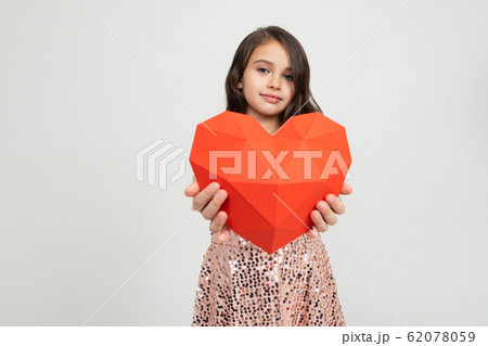 European young girl holding a heart-shaped figure in a studio with light walls 62078059