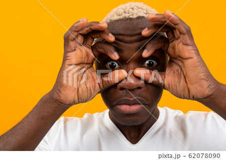 surprised black african young man covers his face with his hands and bulges his eyes on a yellow 62078090