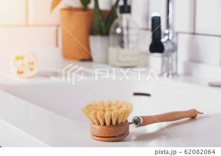 Natural, plastic free brush for washing dishes lying near the sink on modern white minimalist kitchen. Natural, plastic free brush for washing dishes lying near the sink on modern white minimalist kitchen. 62082064