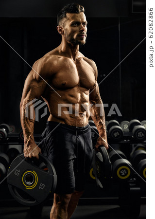 Tensed male bodybuilder holding weights. Tensed male bodybuilder holding weights. 62082866