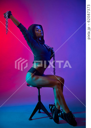Muscular girl holding chain, posing on chair. 62087373