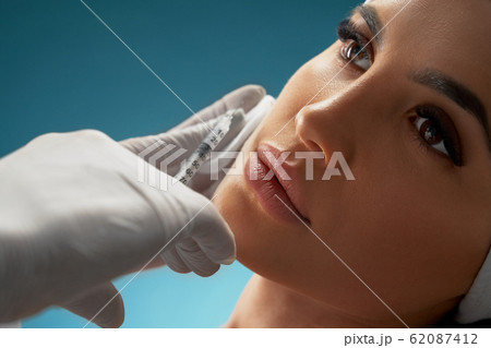 Cosmetologist using syringe to correct female face. 62087412