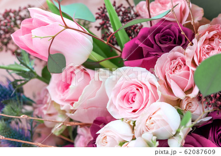 A closeup bouquet of roses and tulips decorated with leaves and twigs of other beautiful plants. 62087609