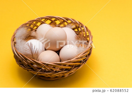 natural ecological eggs and feather in a wicker basket on yellow background with copy space. happy easter natural ecological eggs and feather in a wicker basket on yellow background with copy space. happy easter 62088552