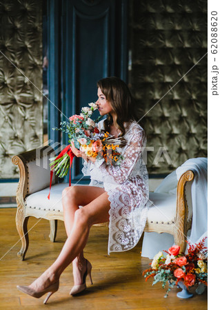 Seductive young bride posing with gorgeous bridal bouquet on a sofa 62088620