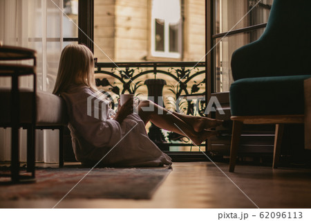 young girl drinks coffee and looks out the window at the city 62096113