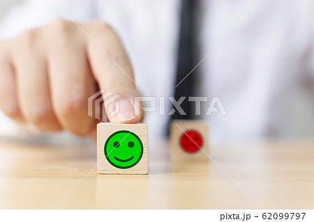 Hand of a businessman chooses a smiley face on wood block cube Hand of a businessman chooses a smiley face on wood block cube 62099797