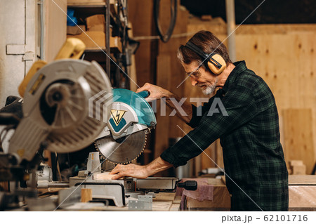 Side view of craftsperson using circular saw over wooden plank at workshop Side view of craftsperson using circular saw over wooden plank at workshop 62101716